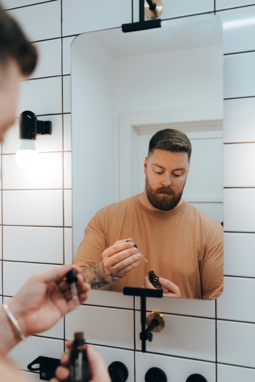 Man applying a hair treatment dropper in front of a bathroom mirror