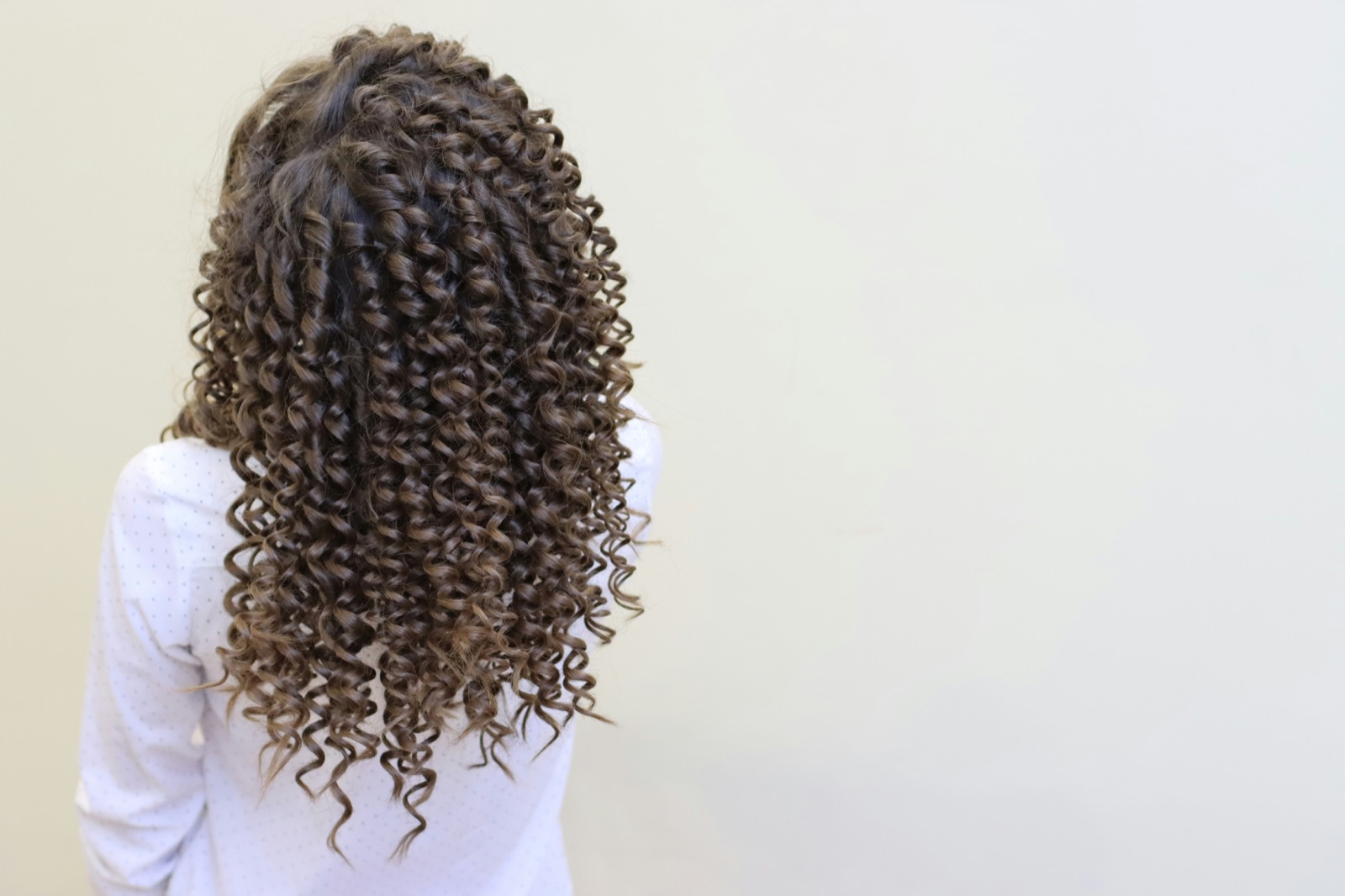 Back view of long, defined curly permed hair against a plain background