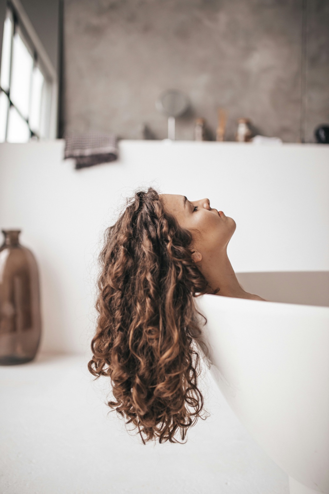 Woman with long permed curly hair leaning back in a bathtub